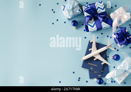 Christmas travel planning. Traveling as gift. White blank model of passenger plane, passports and gift boxes on blue background. Top view or flat lay. Stock Photo