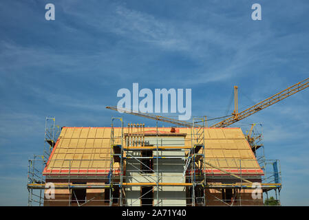 A shell of brick with not yet covered roof and cranes in the background stands against a blue sky with text box Stock Photo