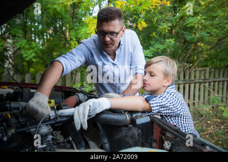 Young father teaching his son to change motor oil in family car. Stock Photo