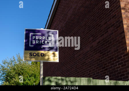 PURPLE BRICKS SOLD sign board next to the brick wall of the house.