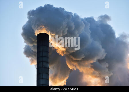 Industrial smoking chimney, against clear sky at sunset. Stock Photo