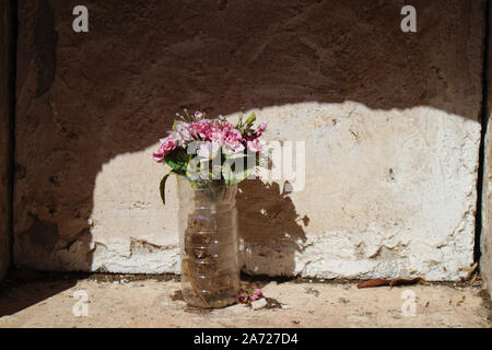 Niche with a simple bouquet of artificial flowers covered in dust in a niche without gravestone Stock Photo