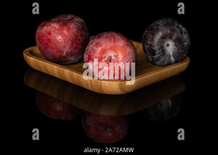 Group of three whole fresh red plum on wooden square plate isolated on black glass Stock Photo