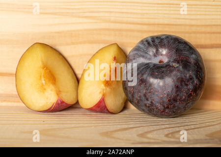 Group of one whole two slices of fresh red plum on natural wood Stock Photo