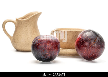Group of two fresh red plums with ceramic jug, cup, saucer isolated on white background Stock Photo