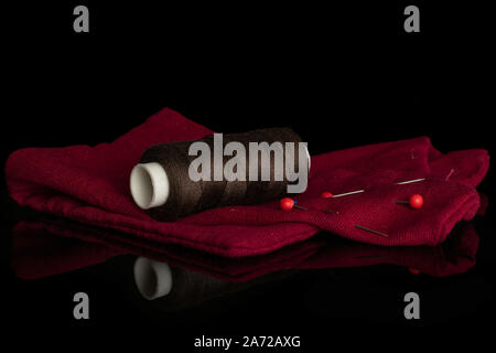 One whole haberdashery item dark brown thread spool with needles on fabric isolated on black glass Stock Photo