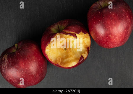 Group of three whole fresh apple red delicious one bitten flatlay on grey stone Stock Photo
