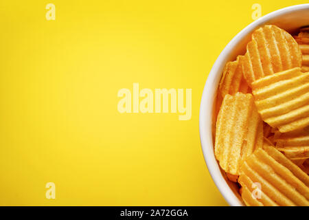 Potato chips fluted, shot from above, very appetizing fried potatoes in a white plate, on a bright yellow background. Close-up, free copy space on the Stock Photo