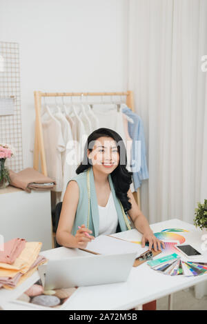 A young Asian fashion designer on her atelier working with a laptop Stock Photo