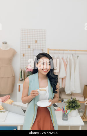 Portrait of beautiful young Asian fashion designer businesswoman at her studio while drinking coffee Stock Photo