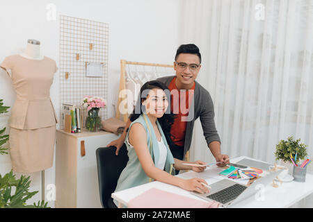 Young female and male fashion designers team talking about new collection, discussing fabrics and patterns for new collection in dressmaker s studio o Stock Photo