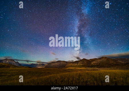 The northern summer Milky Way setting over the mountains of Waterton Lakes National Park, Alberta, Canada, with warm golden lighting supplied by the r Stock Photo