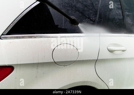 A car washer pointing water on a vehicle body, outdoor cropped shot Stock Photo