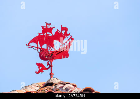 Red colored weather vane depicting a boat with sails stretched by the wind; blue sky background; San Francisco, California Stock Photo