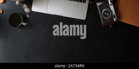 Overhead shot of dark modern workspace with laptop computer, orange notebook with office supplies on black leather desk Stock Photo