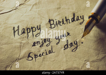 Happy birthday enjoy your special day. Vintage brass pen writing birthday greetings on old paper. Stock Photo