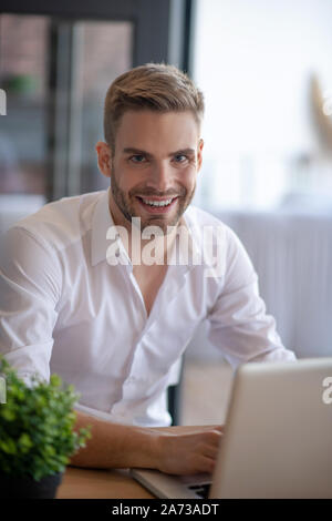 Smiling young handsome businessman sitting near laptop Stock Photo