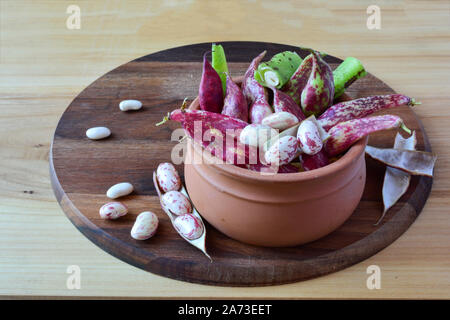 Fresh, organic colorful beans in a clay bowl, on round dark colored walnut chopping board Stock Photo