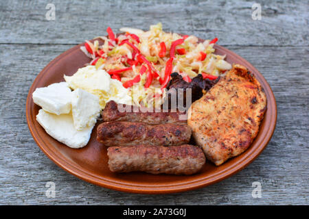 Healthy, tasty and strong dish, chicken steak and liver, cevapcici, dairy products and salad in brown ceramic plate on old oak table, side view Stock Photo