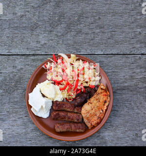 Healthy, tasty and strong dish, chicken steak and liver, cevapcici, dairy products and salad in brown ceramic plate on old oak table, view from above Stock Photo