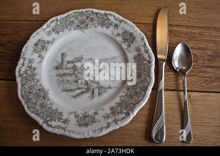 Hand-painted porcelain plate with cutlery on a massive wooden table background Stock Photo