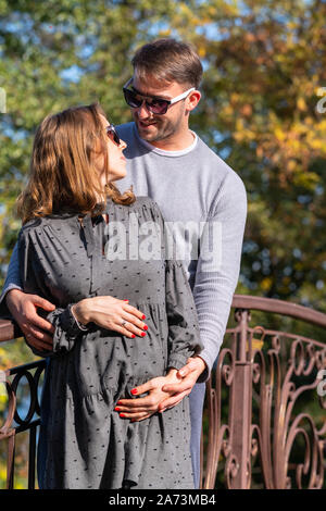 Happy pregnant young woman with her husband standing together in a close embrace cradling her baby bump in their hands Stock Photo