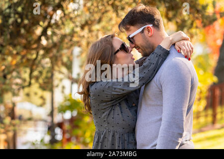 Loving young woman hugging her husband rubbing noses and looking into his eyes in a close up portrait in an autumn park Stock Photo