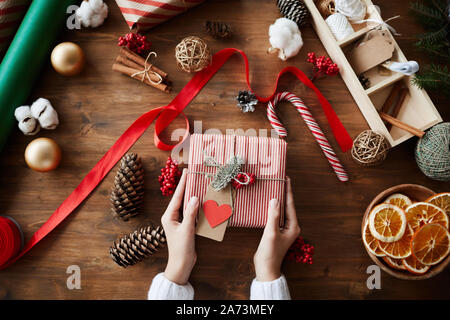Close-up of woman sitting at the wooden table with sweets and decorations and holding decorated Christmas present Stock Photo