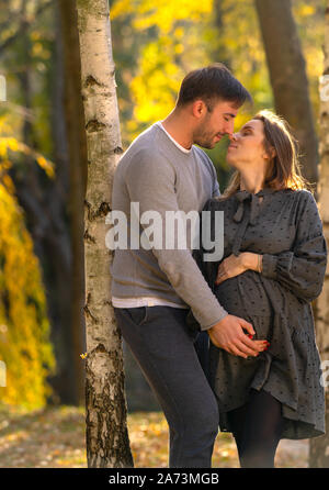 Pregnant woman with her loving husband spending a relaxing evening in an autumn park hugging under a tree Stock Photo