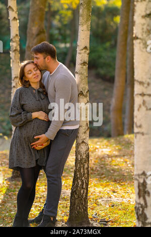 Happy pregnant woman bonding with her husband and unborn child as they relax together in an autumn park between the trees Stock Photo