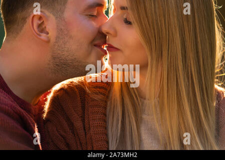 Close up cropped portrait of a loving couple kissing backlit by golden evening light Stock Photo