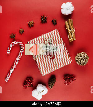 High angle view of gift box decorated in wrapping paper among candies and fir cones isolated on red background Stock Photo