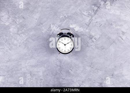 Black vintage clock with alarm on gray concrete background. Flat lay, top view, copy space. Stock Photo