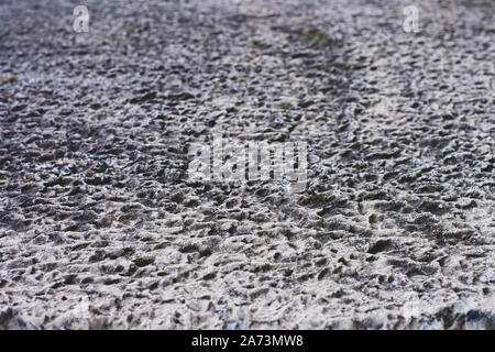 Texture of an old concrete wall with dimples, hollows with outgoing perspective. The porous surface is gray. Selective focus at the beginning. Stock Photo