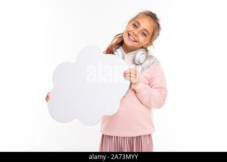 girl in a pink sweater with white headphones on the neck on a white isolated background, the child holds an empty cloud in his hands for text Stock Photo
