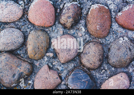 Texture of beautiful large natural multi-colored stones in concrete on the road. The stones are old with cracks and chips. Stock Photo