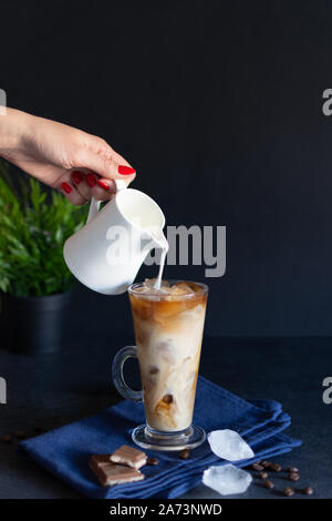 Iced coffee in a tall glass with cream poured over. Cold coffee with cubes of ice and cream. Stock Photo