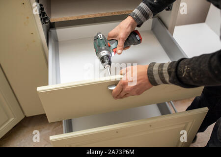 Man using electronic drill to install a cabinet Stock Photo