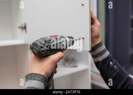 Man using electronic drill to install a cabinet Stock Photo