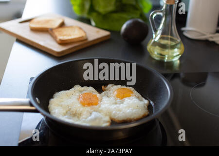 Preparing early morning eggs breakfast on modern induction stove in home kitchen. Stock Photo