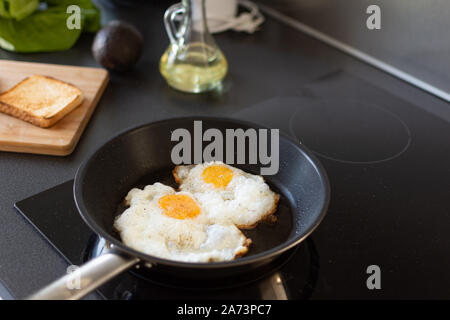 Preparing early morning eggs breakfast on modern induction stove in home kitchen. Stock Photo