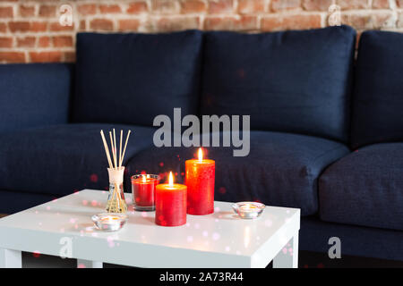 Room air refresher sticks and red burning candles on table on home modern interior. Stock Photo