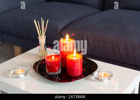 Room air refresher sticks and red burning candles on table on home modern interior. Stock Photo