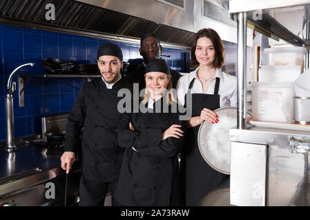 Positive multinational team of restaurant staff standing together in professional kitchen Stock Photo