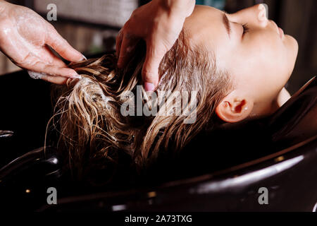 Hair stylist washing hair to the customer before doing hairstyle. Hairdresser applying nourishing mask on woman's hair in beauty salon. Hair wash sham Stock Photo