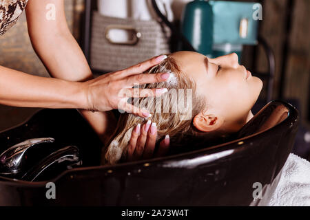 Hair stylist washing hair to the customer before doing hairstyle. Hairdresser applying nourishing mask on woman's hair in beauty salon. Hair wash sham Stock Photo