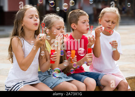 cheerful smiling boy and girls in elementary school age blowing bubbles outdoors Stock Photo