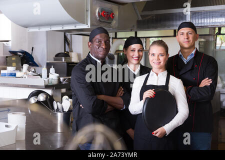 Successful multinational team of restaurant staff standing together in professional kitchen Stock Photo