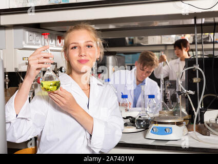Attractive female student performing experiments in university laboratory, examining chemical substances in glass lab flask Stock Photo