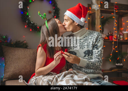 A man makes a marriage proposal to his girlfriend giving her an engagement ring on Christmas eve in a cozy home environment. The best new year gift. Stock Photo